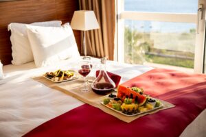 A hotel guest in pajamas sits at a small table in their room, enjoying a meal delivered on a tray.