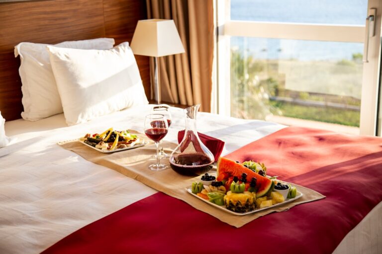 A hotel guest in pajamas sits at a small table in their room, enjoying a meal delivered on a tray.